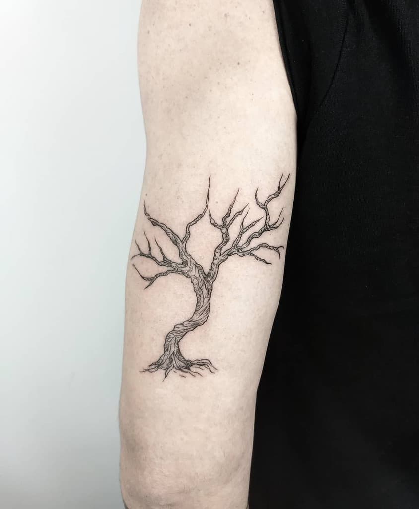 Black and white tattoo of an intricate, leafless tree with twisted branches on an upper arm