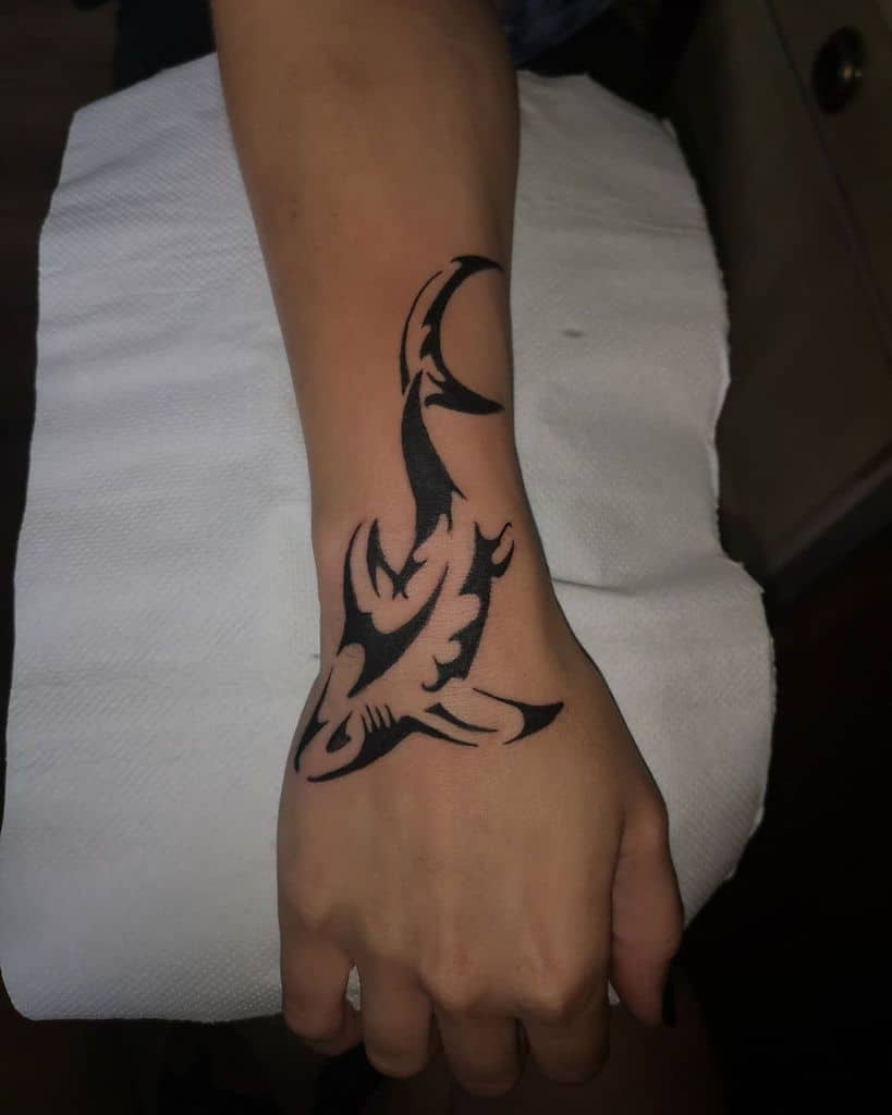 A tribal shark tattoo graces the forearm