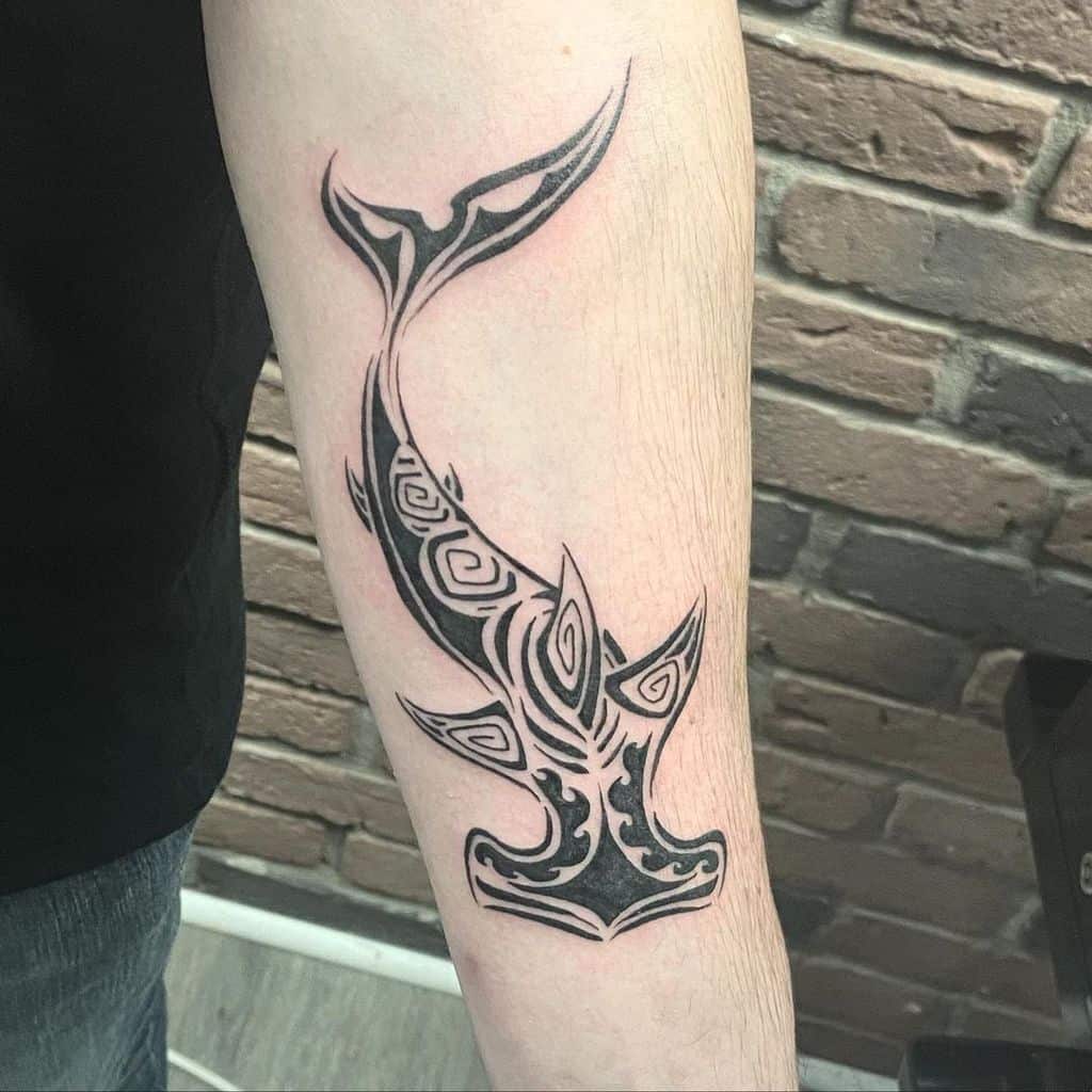 A striking tribal hammerhead shark tattoo gracefully adorns a person's arm, its intricate design weaving seamlessly with the natural flow of the body