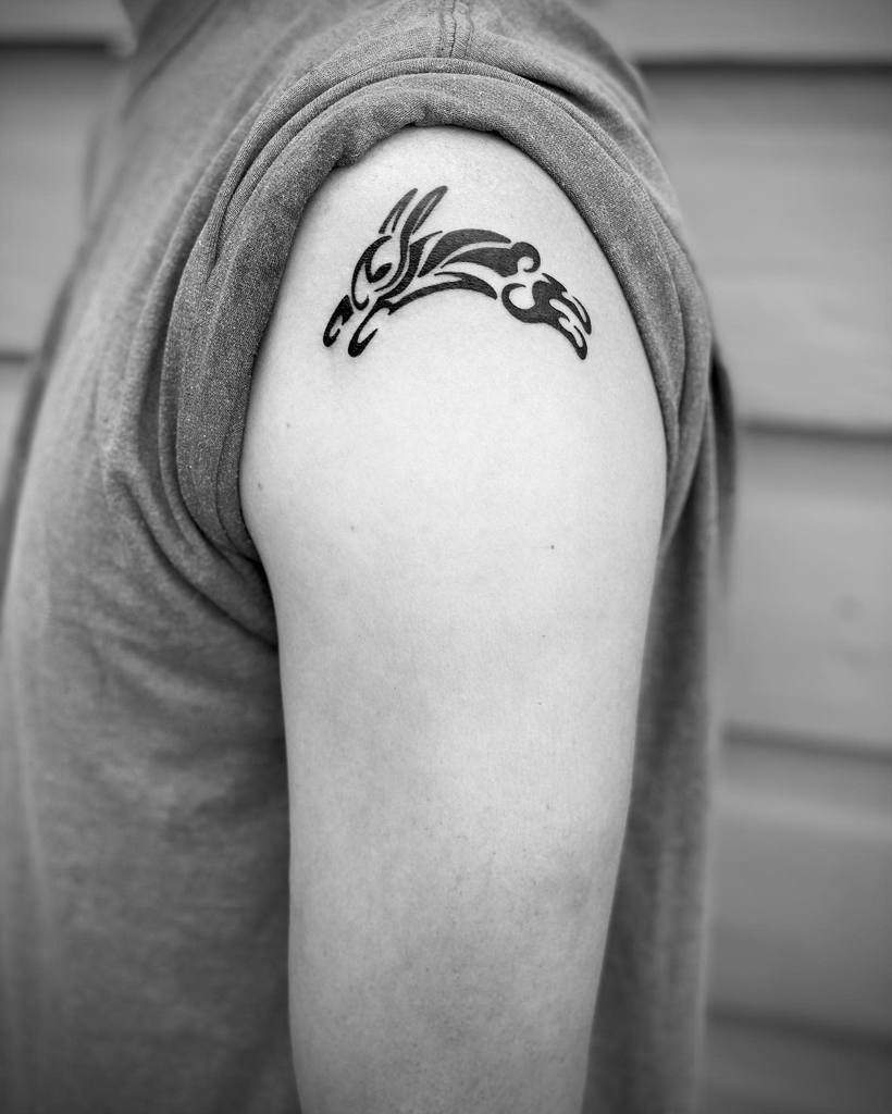 An arm adorned with a small tribal-style rabbit tattoo, skillfully rendered in bold black ink