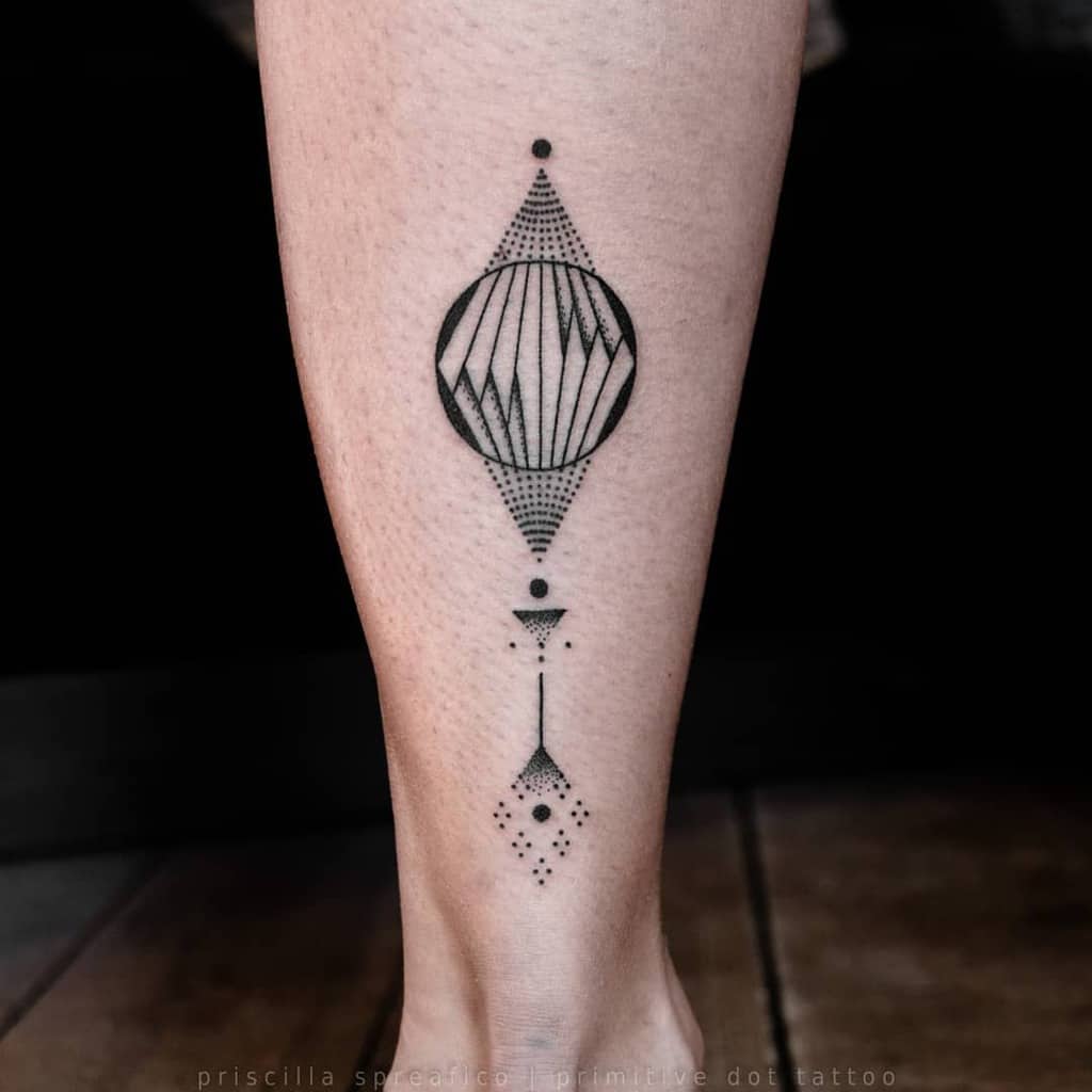 Small leg tattoo features a geometric design with a central circular shape, surrounded by triangles and dotted patterns, creating a modern, minimalistic look