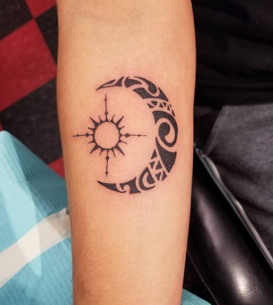 This small tribal tattoo features an intricate crescent moon and sun design elegantly wrapped around the arm