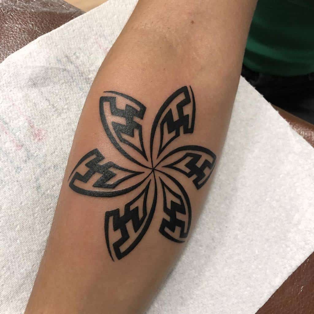 Arm tattoo of a black geometric star pattern resembling a tribal flower