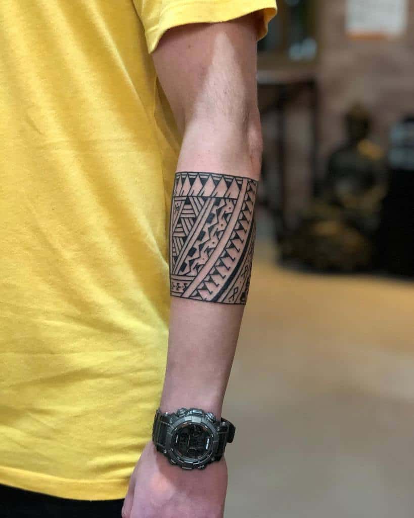 The tattoo features a bold tribal design covering the forearm, with intricate geometric patterns, sharp lines, and symmetry