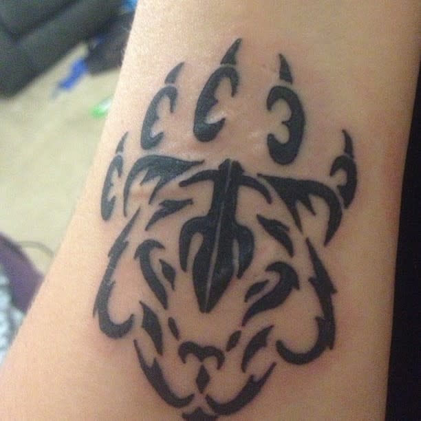 A black tribal tattoo design on skin, resembling the face of a tiger with abstract curves and lines intertwined with hints of a bear's fierce gaze
