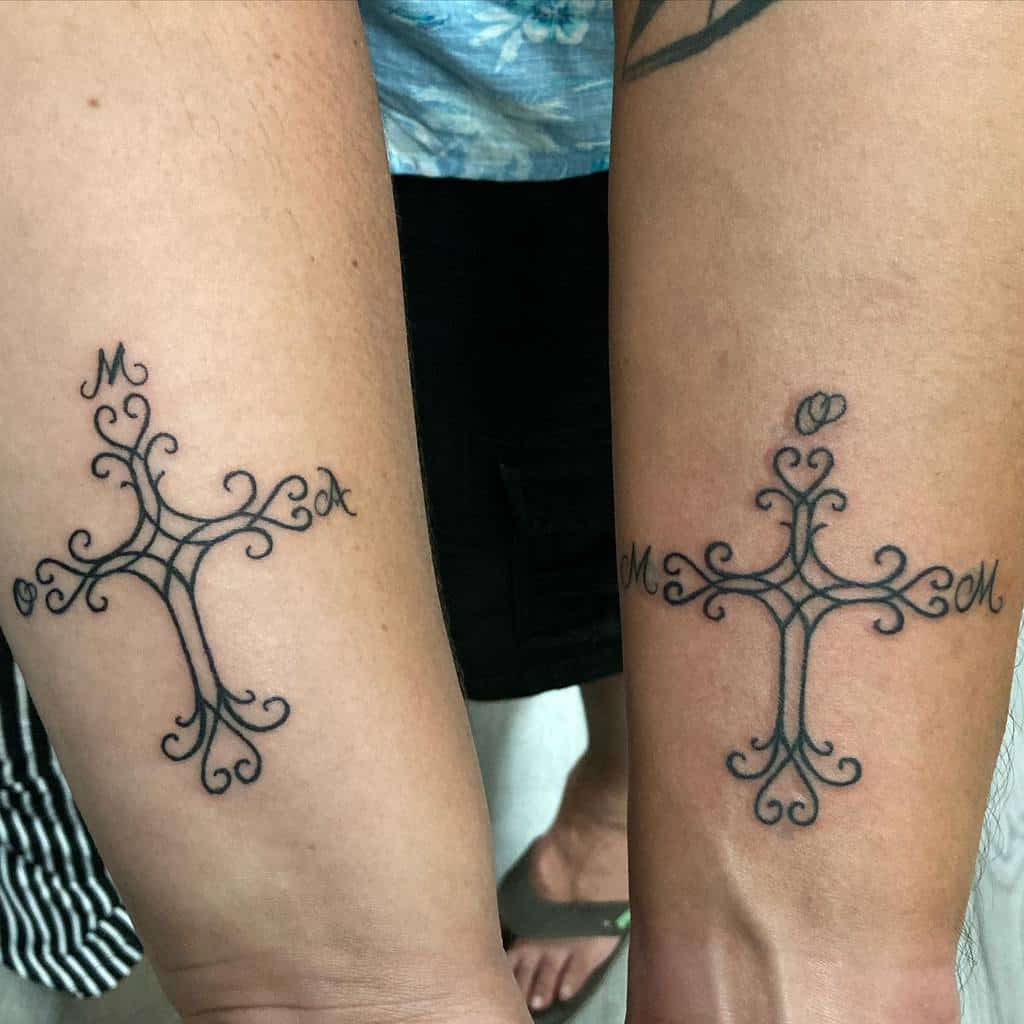 Matching tribal cross tattoos on two forearms with intricate linework and initials, symbolizing unity and connection