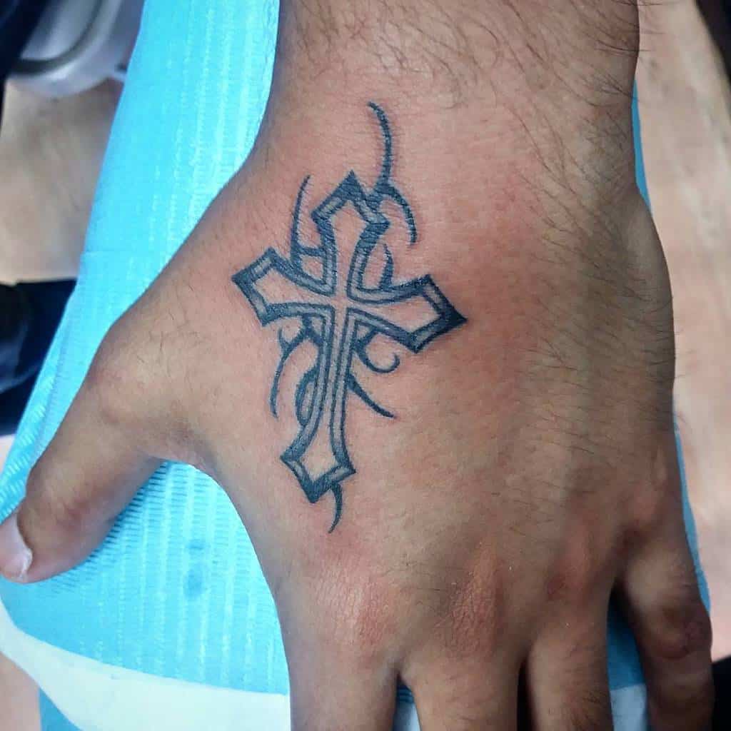A hand tattoo featuring a stylized cross intricately entwined with tribal designs