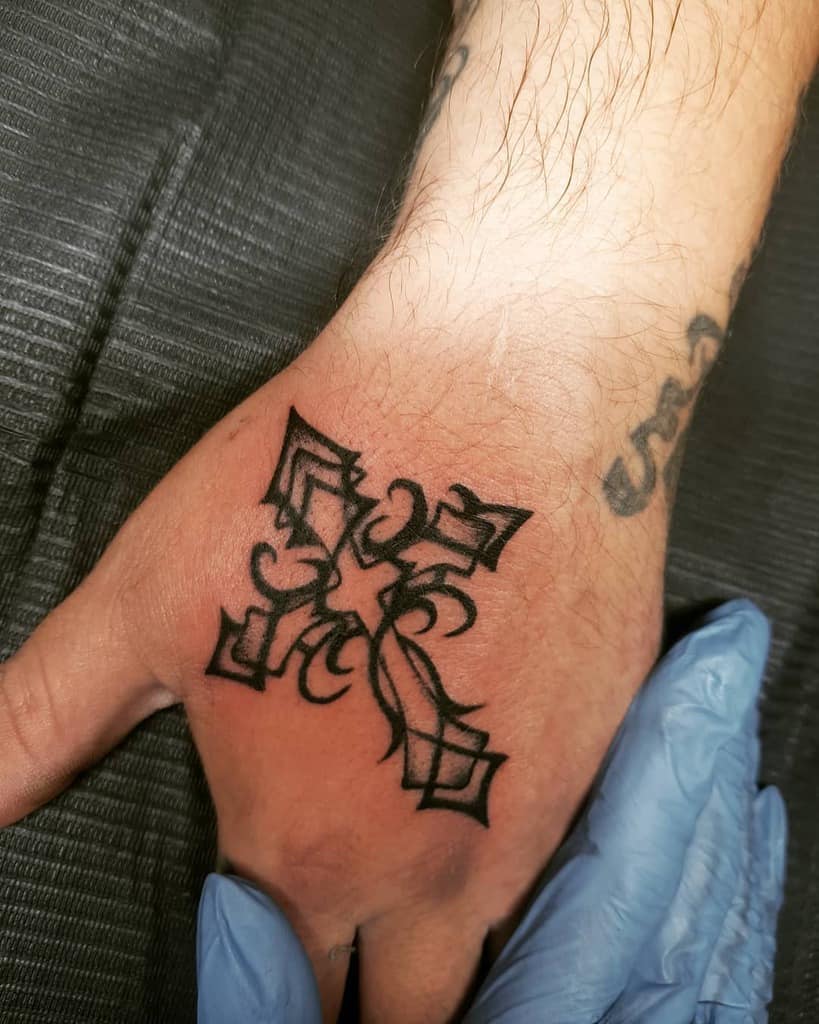 Tattoo of a black ornamental cross on the back of a hand
