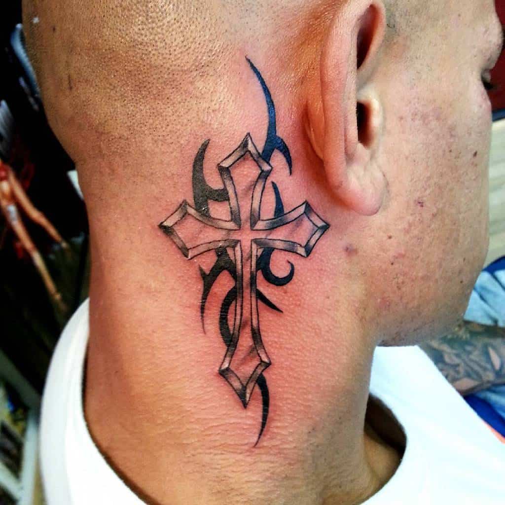Tattoo of a cross with tribal designs on the side of a person's neck