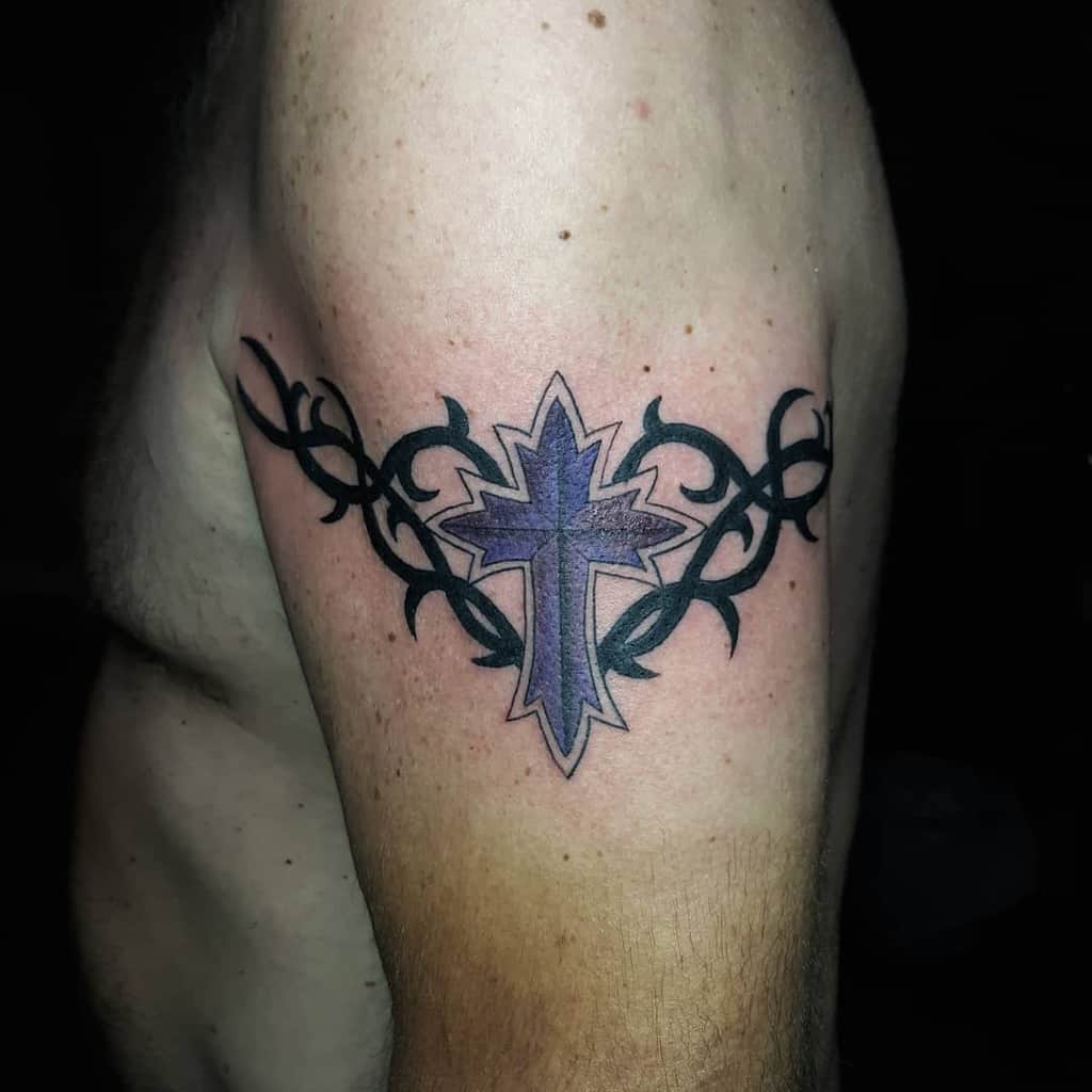 A striking tattoo features a powerful purple cross intertwined with an intricate black tribal design on a man's upper arm