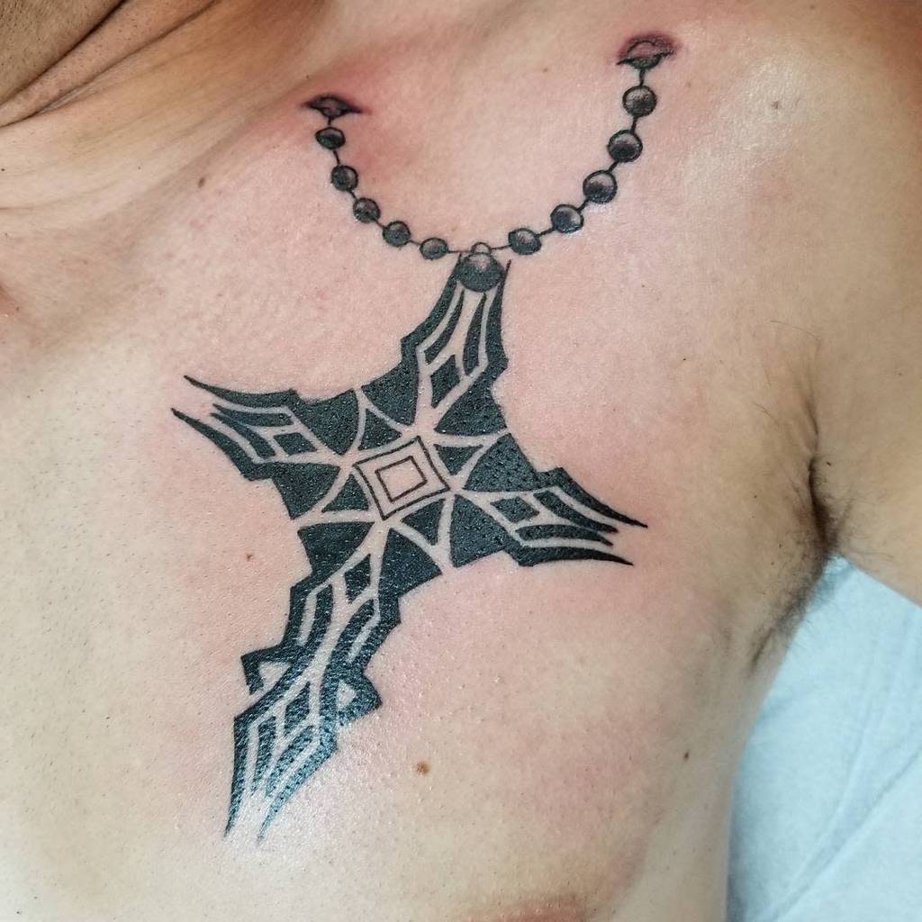 Tattoo of a black shuriken intertwined with a chain, detailed with geometric patterns and subtly incorporating cross elements on a person's chest