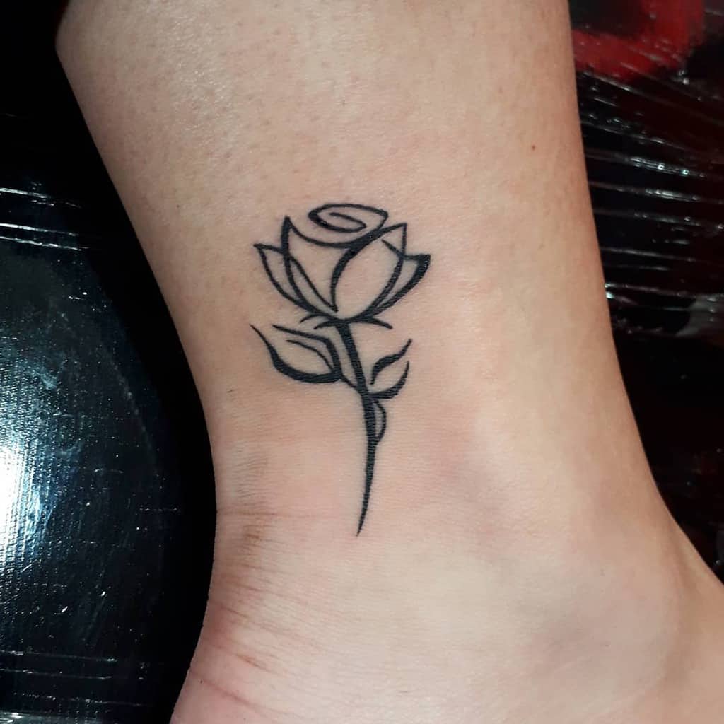 Minimalist black rose tattoo on ankle with a simple stem and leaves design