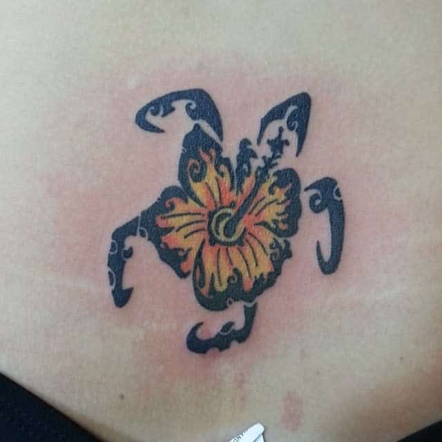 Unique turtle-shaped tattoo featuring tribal patterns with a vibrant yellow hibiscus flower at the center for a tropical vibe