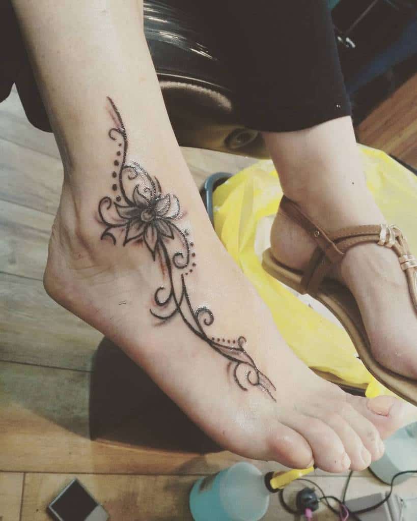 Foot tattoo with a floral and swirl design, featuring black ink accents and dot details