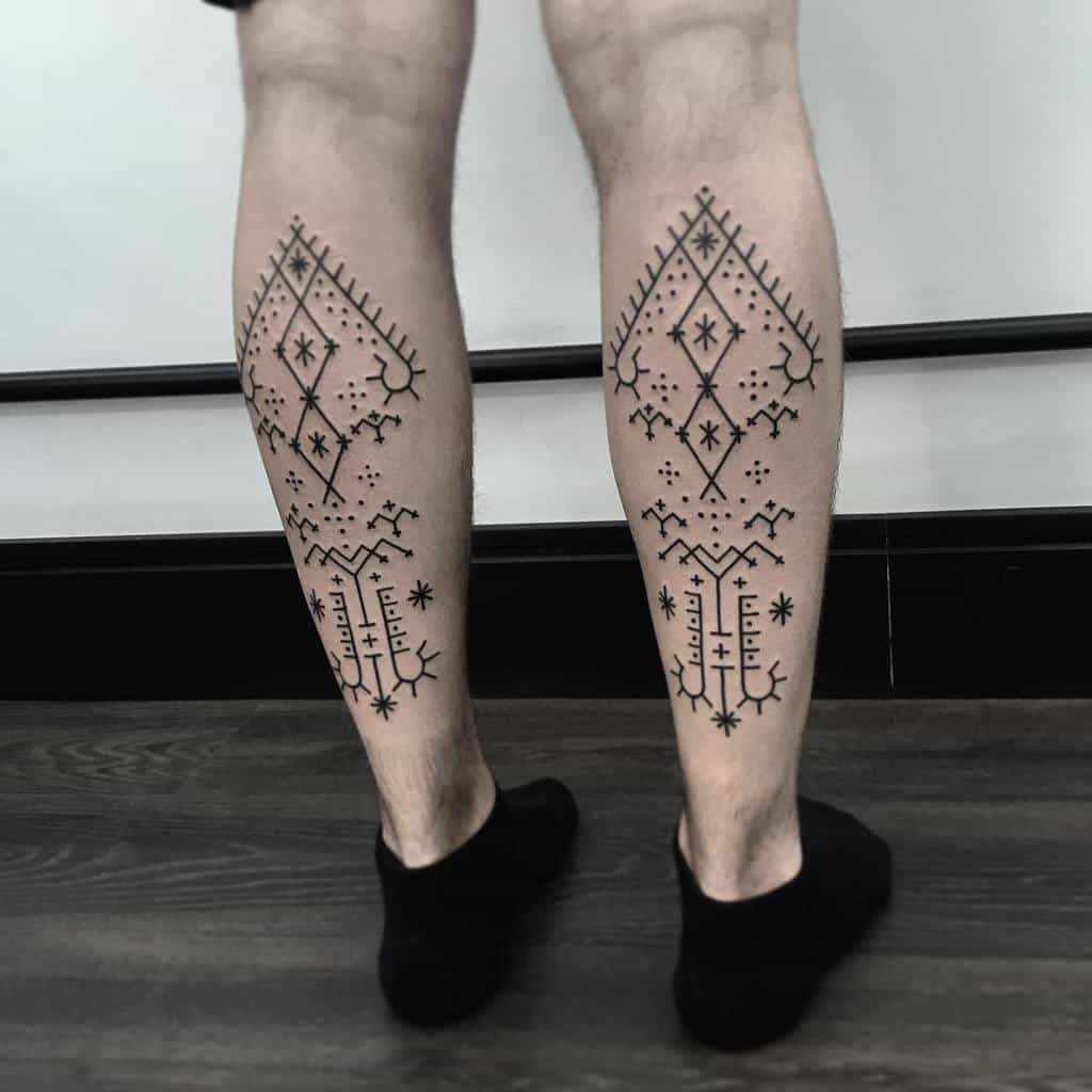 The tattoo features intricate tribal designs on both legs, with geometric patterns, crosses, stars, and symbolic elements arranged symmetrically down each calf for a bold, cohesive look