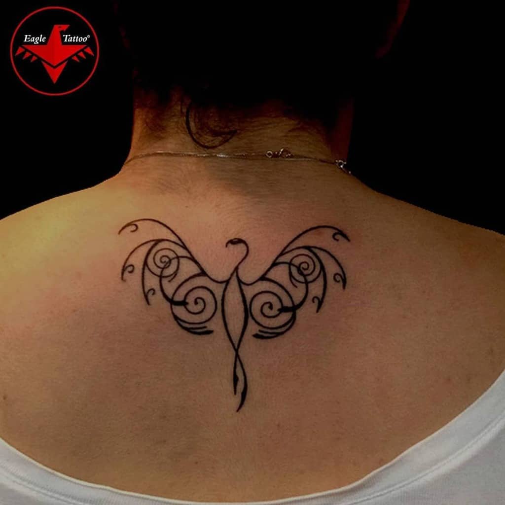 A tribal-style phoenix tattoo on the upper back, featuring swirling lines and elegant, flowing wings
