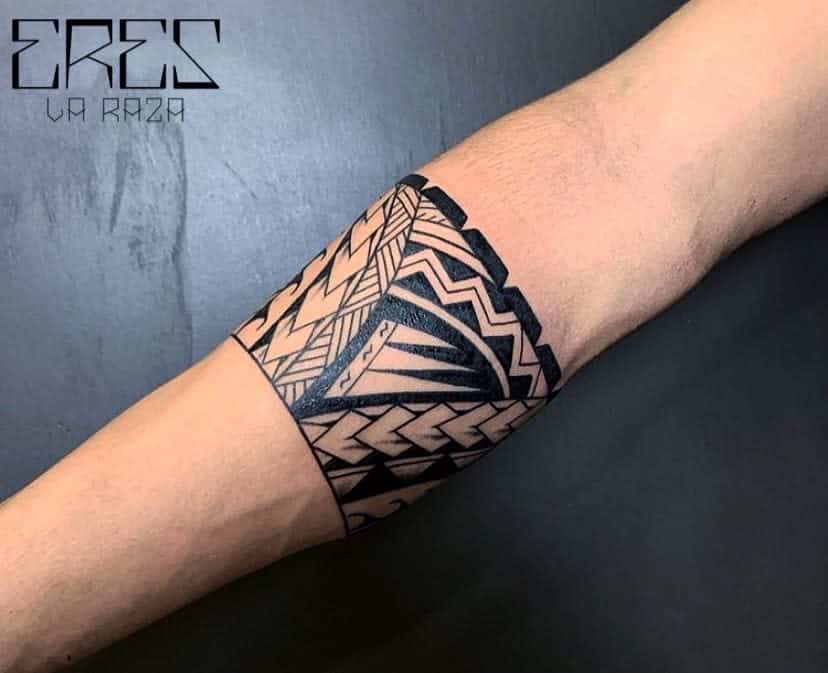 The tattoo features a bold Polynesian-inspired design on the forearm, with intricate geometric patterns, sharp lines, and a symmetrical layout, creating a striking visual impact
