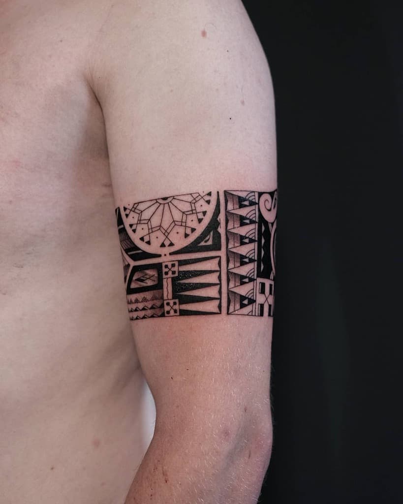 The tattoo features a detailed Polynesian-style design wrapping around the upper arm, with intricate geometric patterns, sharp lines, and bold black ink creating a visually striking and symmetrical composition