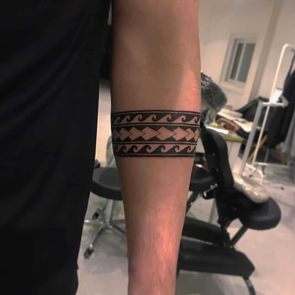 Forearm adorned with a tribal-inspired geometric black armband tattoo, featuring intricate wave patterns