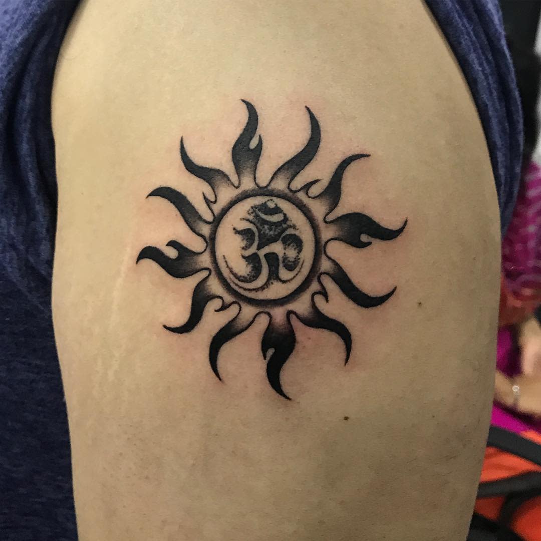 Tattoo of a tribal-style sun with an "Om" symbol at its center on an upper arm