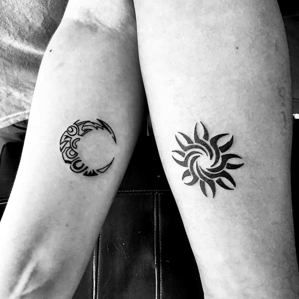Tribal-style crescent moon tattoo on left arm and sun with swirling rays tattoo on right arm