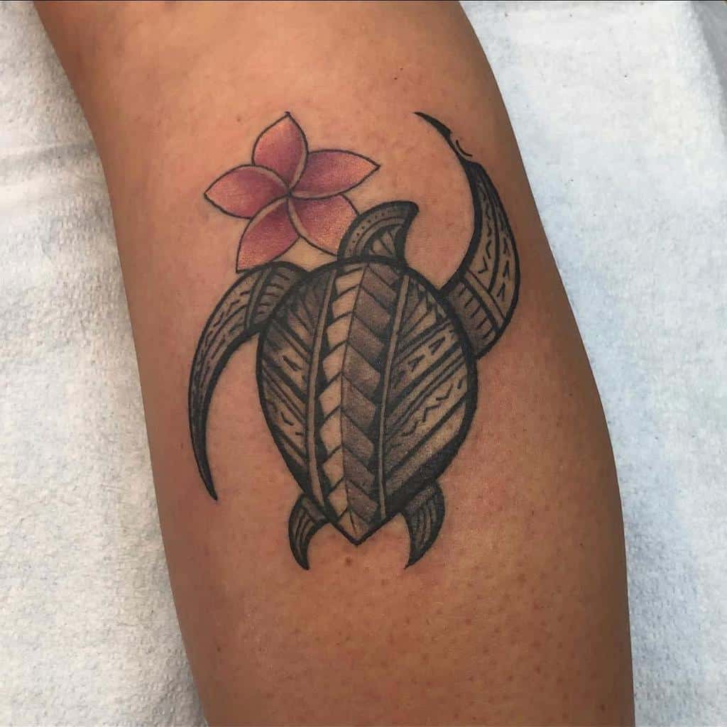 Turtle tattoo with tribal patterns and a pink flower above on an arm