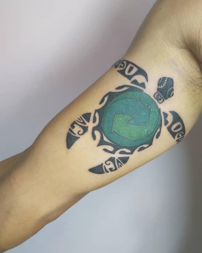 A tribal-style turtle tattoo featuring a green shell with a recycling symbol, accented by black tribal patterns on the flippers and body