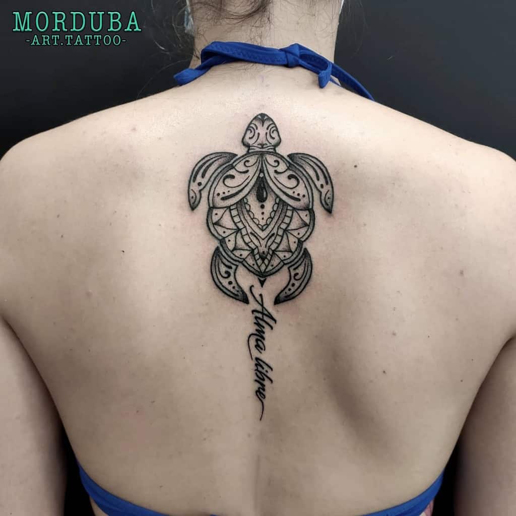 A tribal turtle tattoo with intricate geometric patterns, located on the back, with the phrase "Alma Libre" written beneath