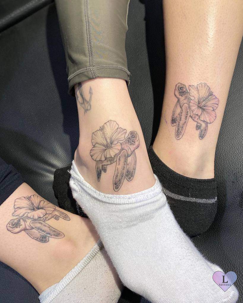 A delicate black ink tattoo of a turtle intertwined with a hibiscus flower, placed on the ankle