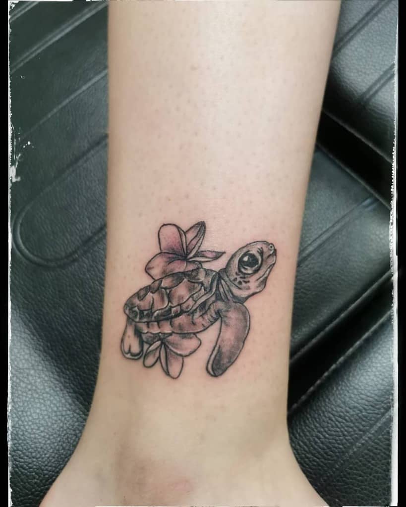 A black and grey tattoo of a turtle swimming alongside a flower, located on the ankle