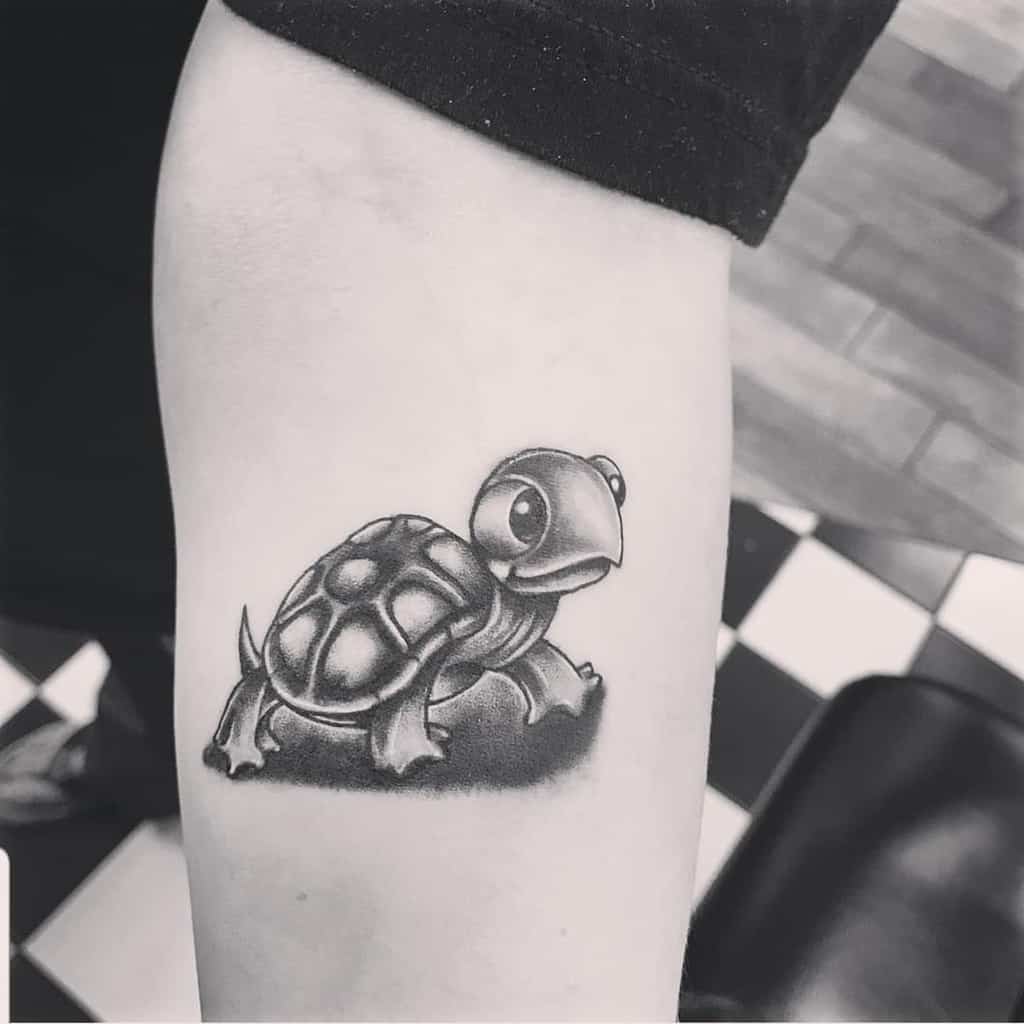 Black and white tattoo of a cartoon turtle on a forearm