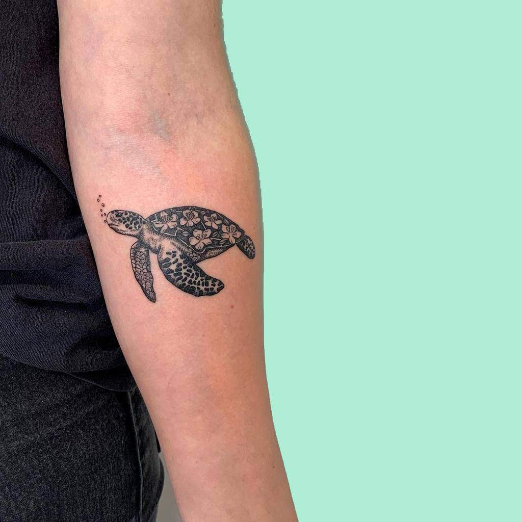 Tattoo of a sea turtle with floral patterns on a forearm 
