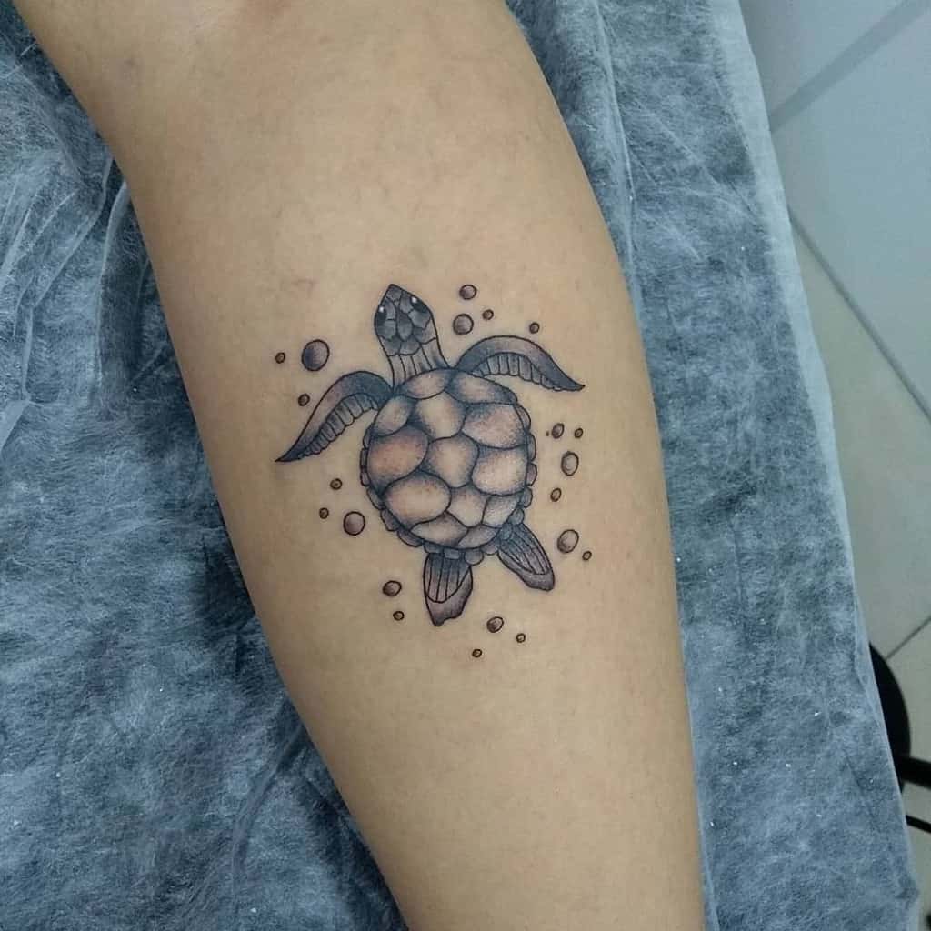 A black and grey tattoo of a turtle surrounded by bubbles, inked on the forearm