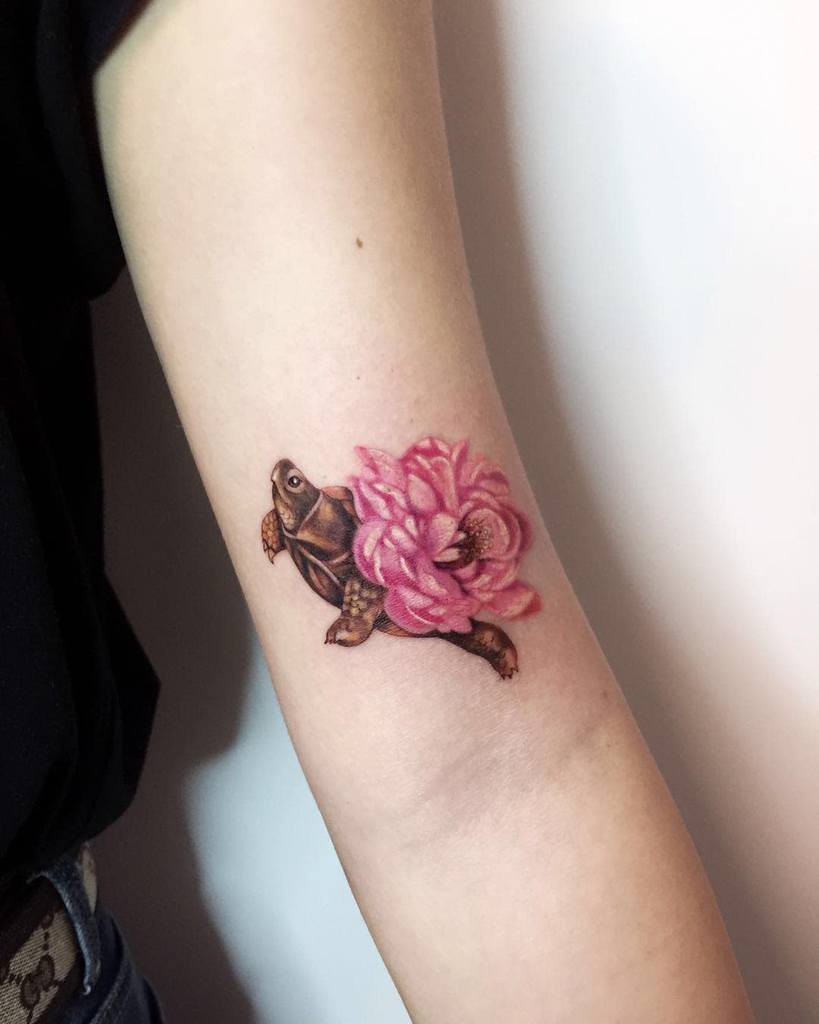 Tattoo of a turtle with a pink flower on an arm