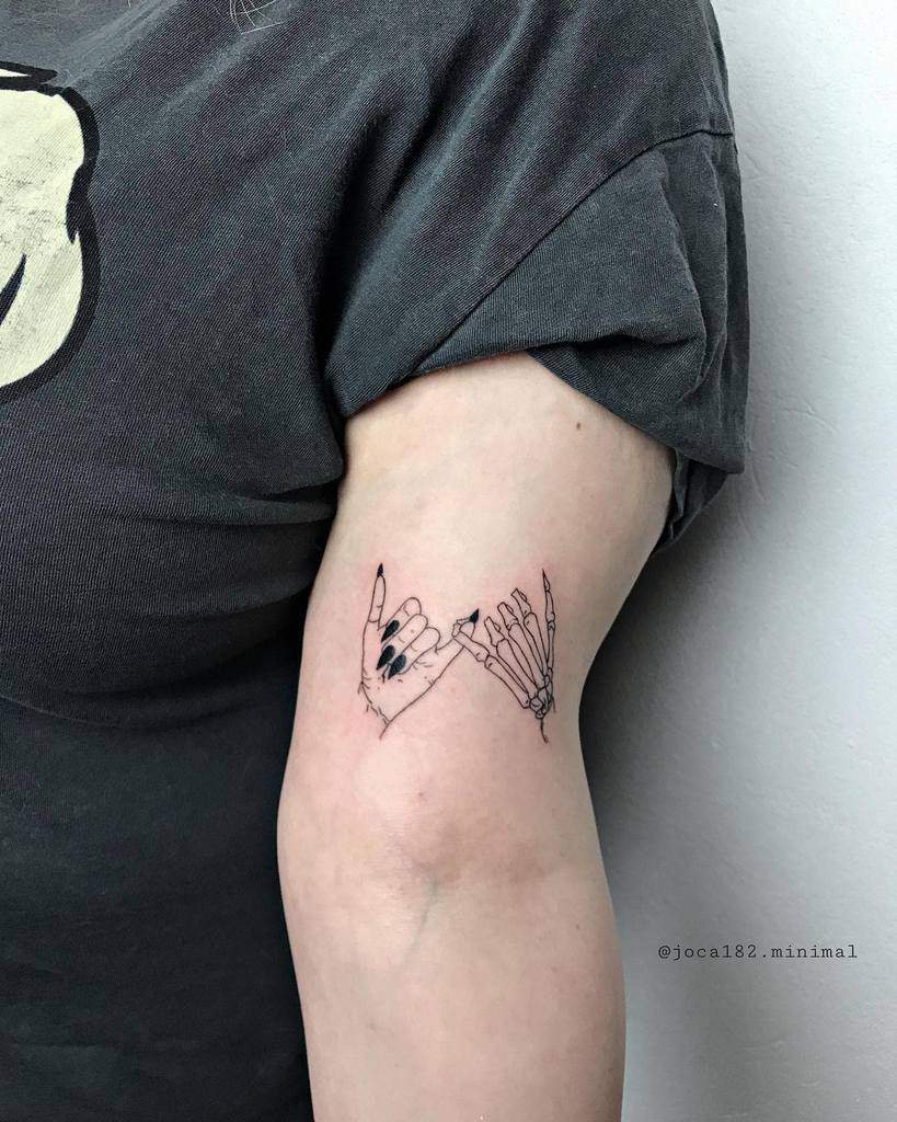 Line art tattoo of linked human and skeletal hands on an upper arm