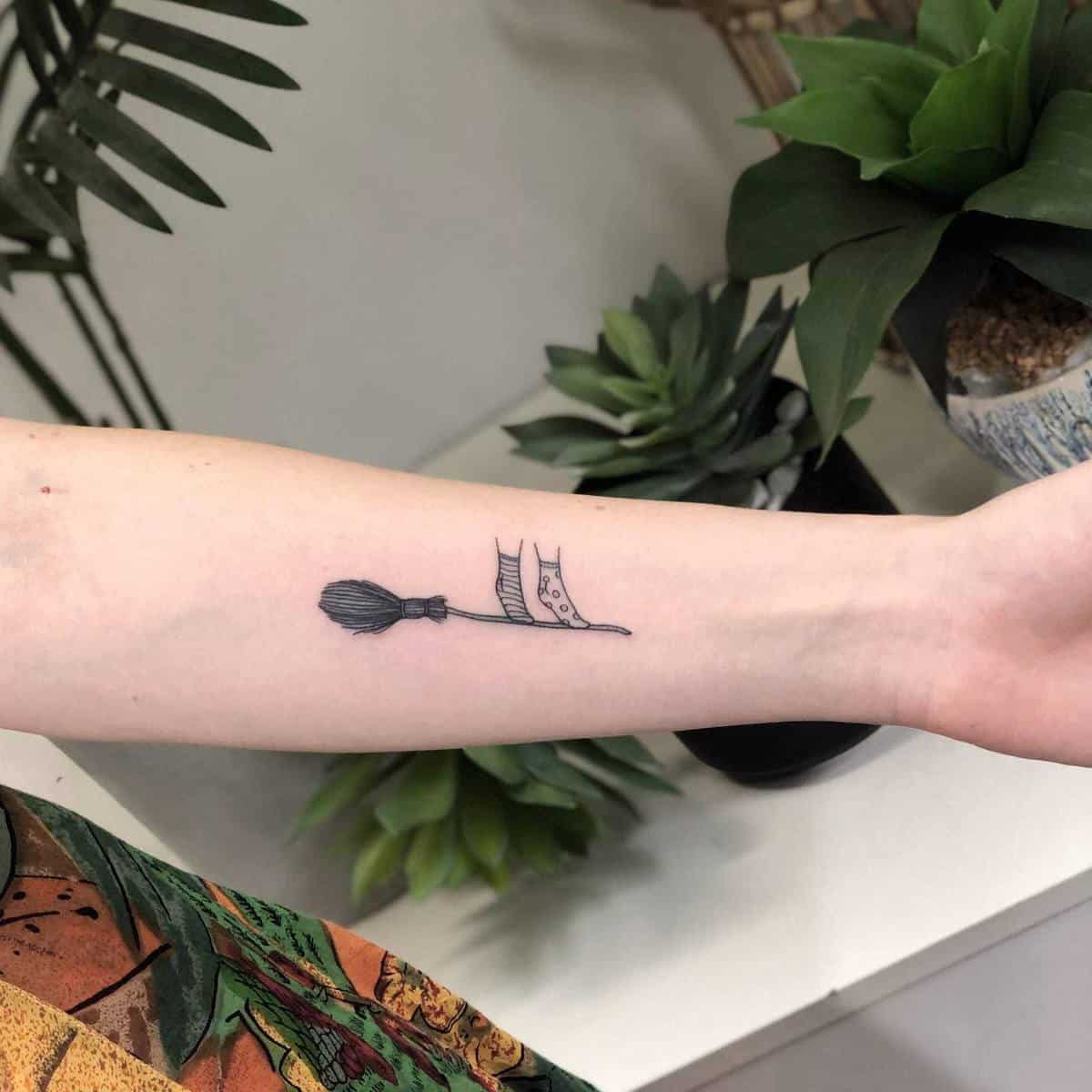 Forearm tattoo of a broomstick with someone wearing socks standing on it