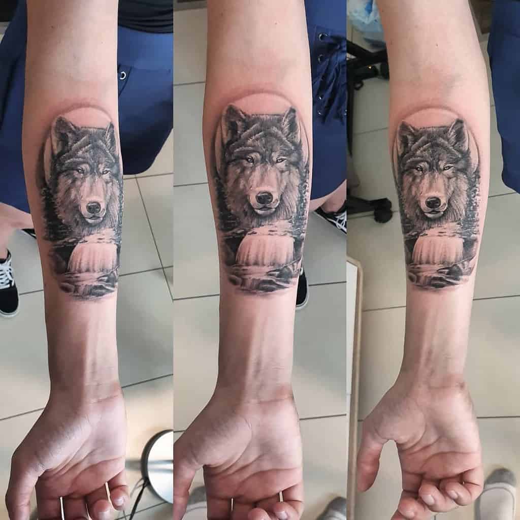 Realistic wolf tattoo on the forearm, featuring a serene waterfall background and intricate shading details