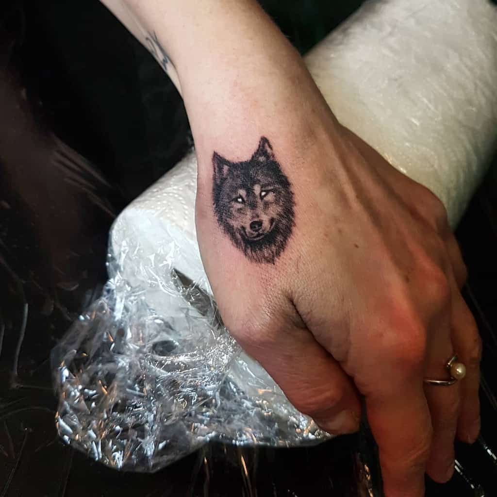 Small and detailed wolf head tattoo on the back of the hand, featuring fine shading for a realistic effect