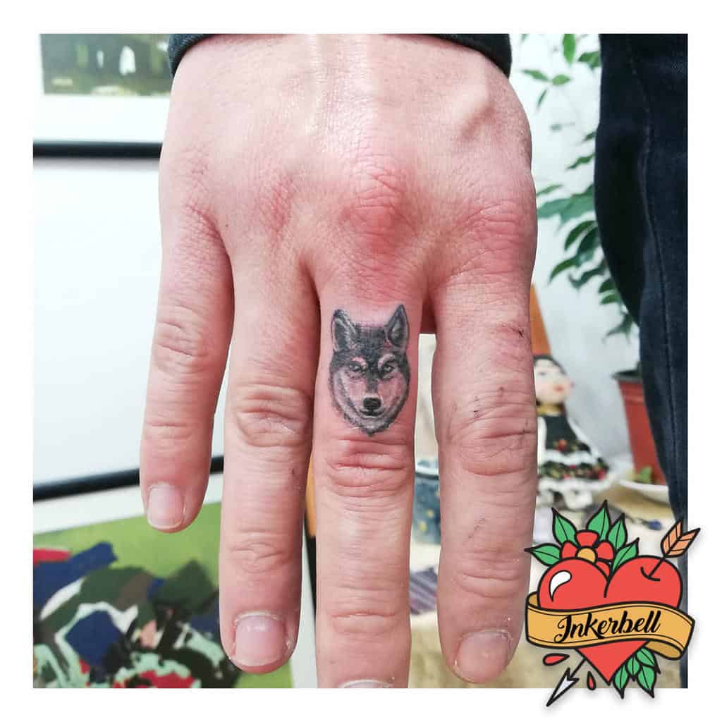 Miniature wolf head tattoo on the middle finger, showcasing precise details and a bold design for a striking look