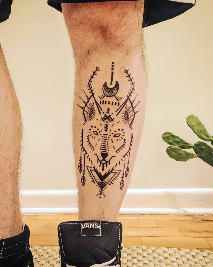 Intricate wolf tattoo on the calf, featuring tribal-inspired patterns, geometric shapes, and feather details