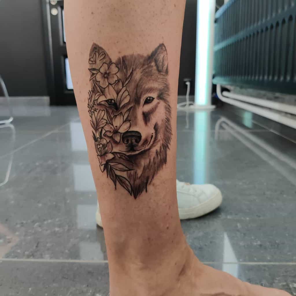 A stunning wolf and floral tattoo graces the calf