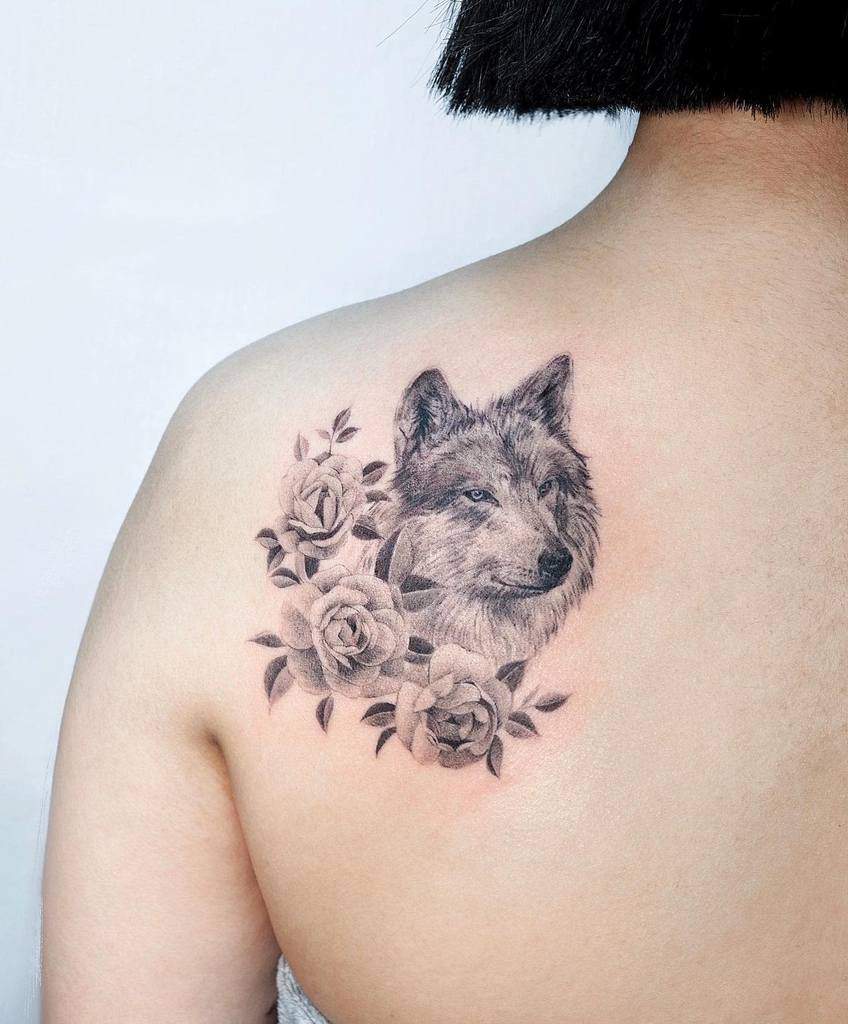 A stunning tattoo of a wolf majestically surrounded by roses adorns the person's upper back