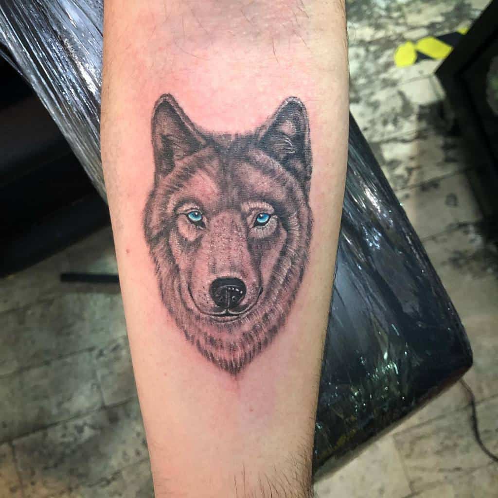 A striking tattoo of a wolf graces the forearm, its piercing blue eyes capturing attention