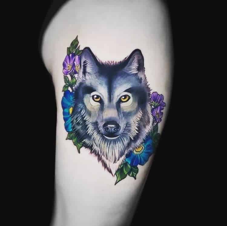 Tattoo of a majestic wolf encircled by vibrant purple and blue flowers on an arm