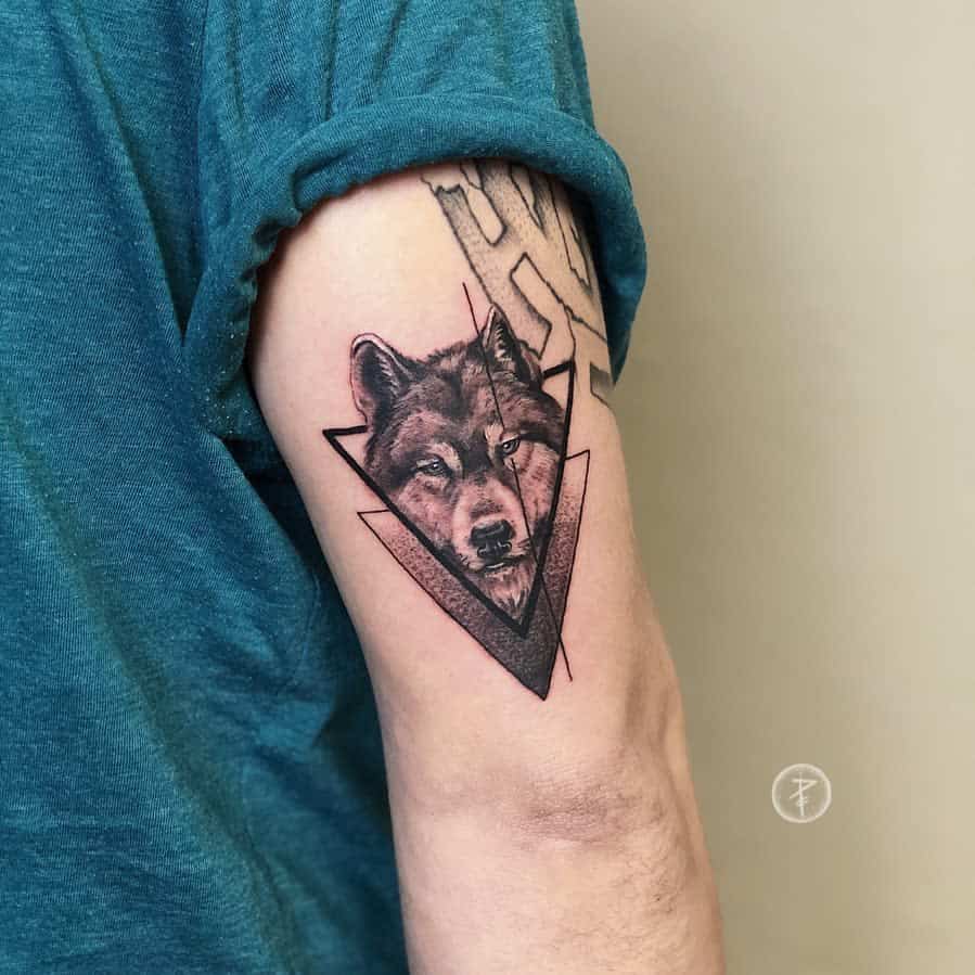A geometric triangle frames a striking wolf tattoo on a person's upper arm, merging artistry with the spirit of the wild