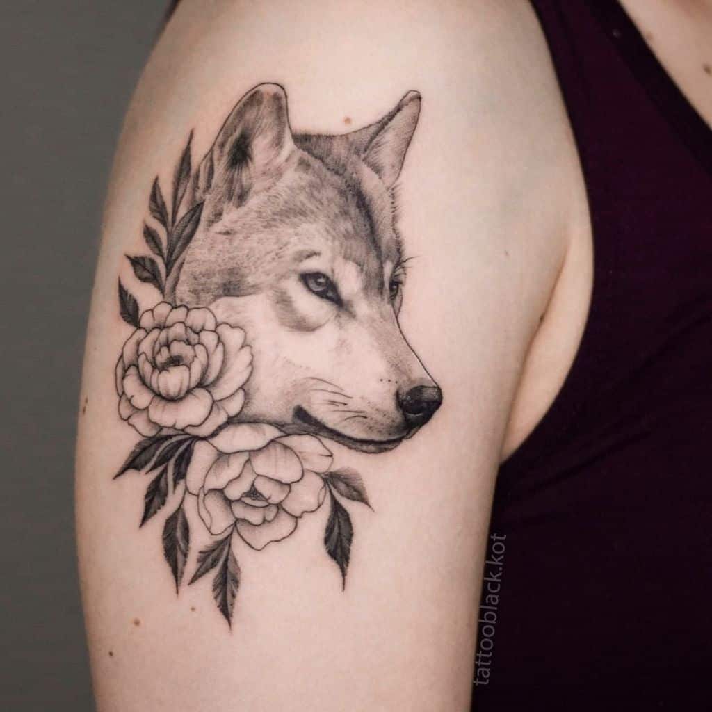 This stunning tattoo features a majestic wolf head intertwined with elegant roses and leaves, beautifully crafted on the upper arm
