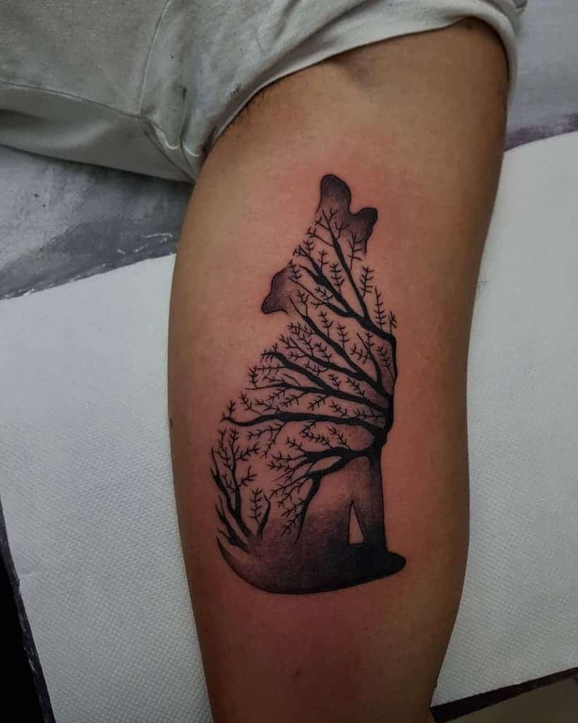 A tattoo of a wolf silhouette intertwined with tree branches elegantly graces a person's arm