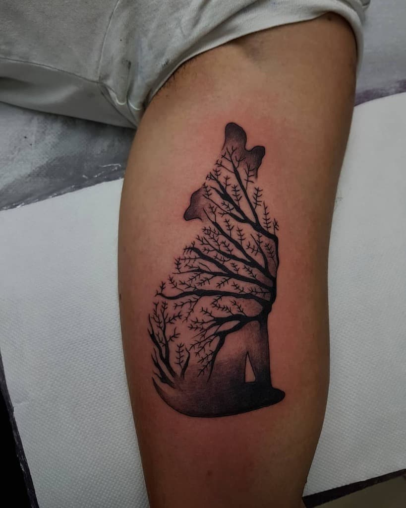 A striking tattoo of a wolf silhouette intricately filled with tree branches adorns the arm