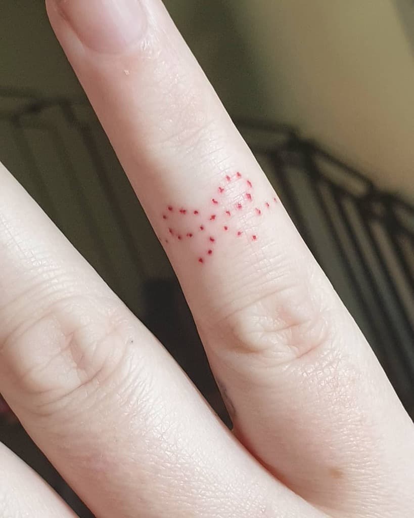 Hand with a small dotted red bow tattoo on the finger