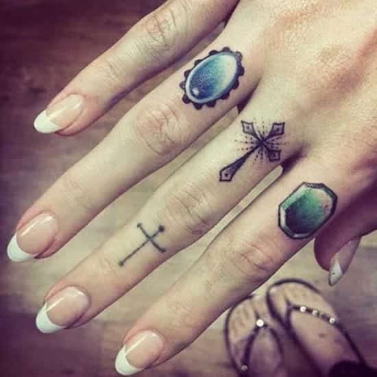 Hand with various small tattoos, including crosses and a jewel design on fingers